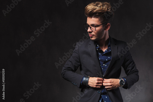 elegant man wearing glasses while fixing his jacket in dark stud