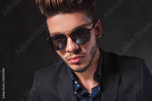 fashionable man posing at the camera wearing sunglasses in studi