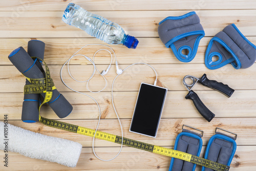 Sport Equipment. Dumbbells, Ankle Weights, Wrist Weights, Hand Grip, Towel, Tape Measure, Bottle Of Water, Smart Phone With Earphones On Boards. Sport Fitness Background