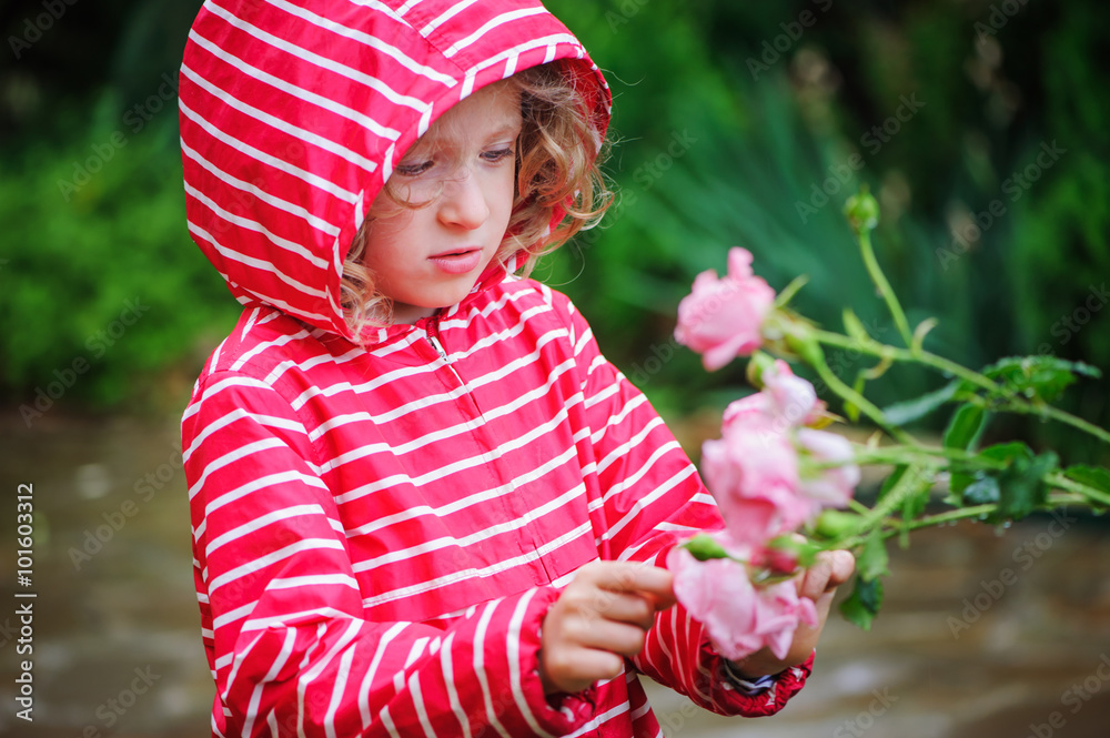 Φωτογραφία child girl in red striped raincoat playing with wet roses in rainy summer garden
