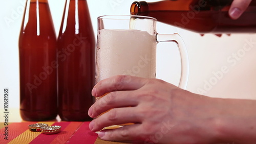 Man hand holding brown bottle and refilling mug with beer
 photo