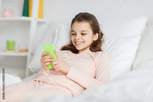 happy girl lying in bed with smartphone at home
