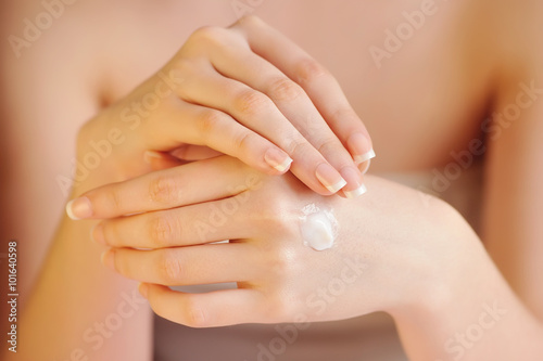 Young woman applies cream on her hands after bath. Focus on hand