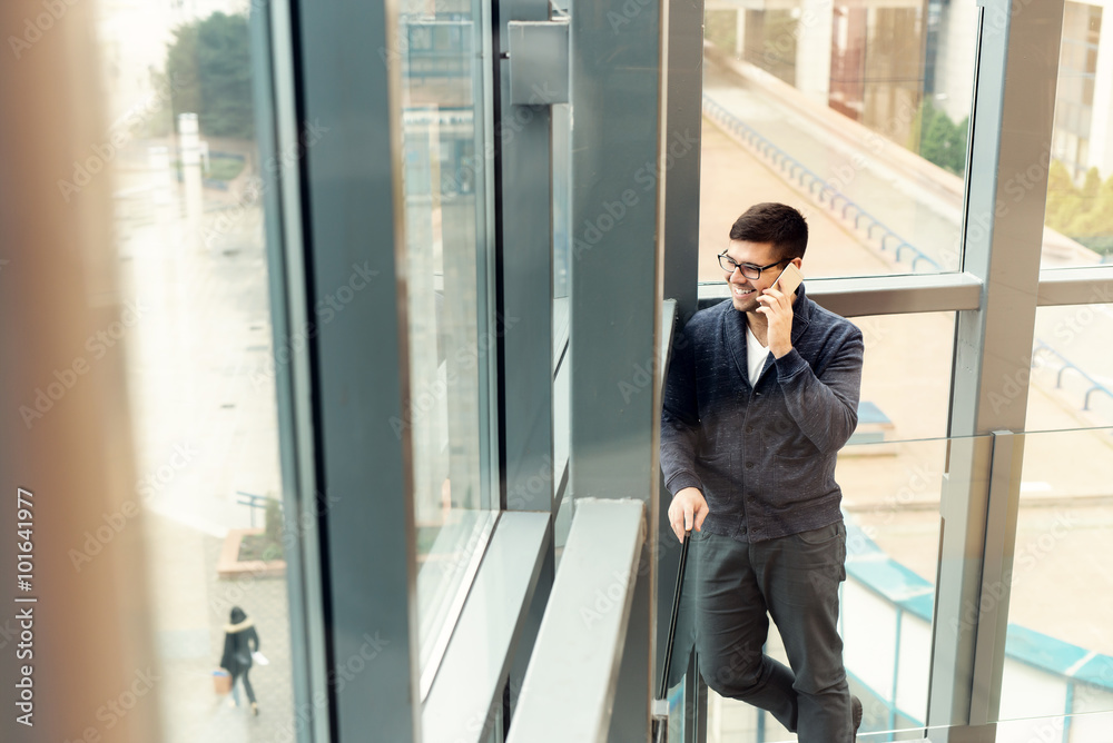 Casual businessman talking on smart phone. He is standing in front of a big window and looking outside. Casual businessman talking on smart phone. He is standing in front of a big window and looking outside.