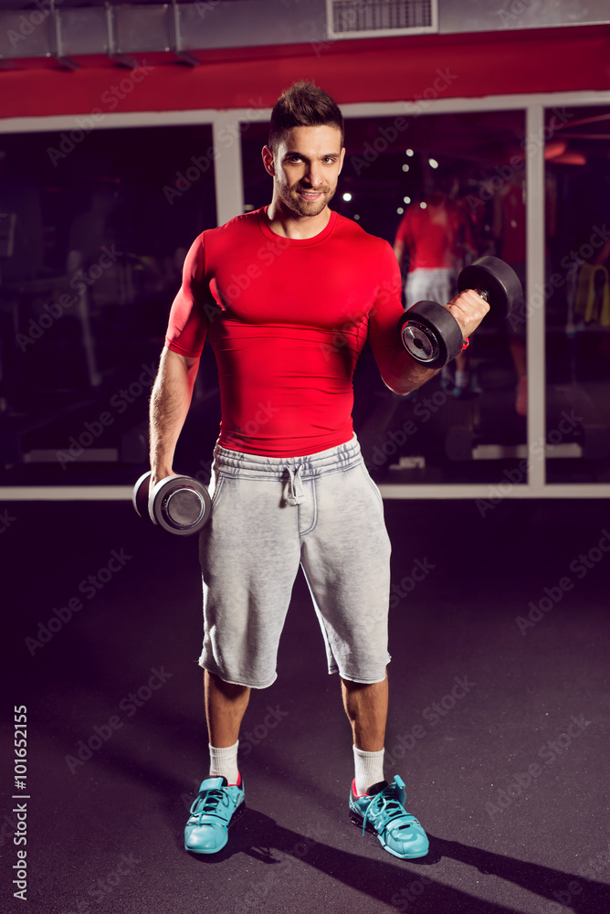 Handsome muscular man working with dumbells at gym.