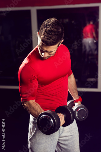 Handsome muscular man working with dumbells at gym.