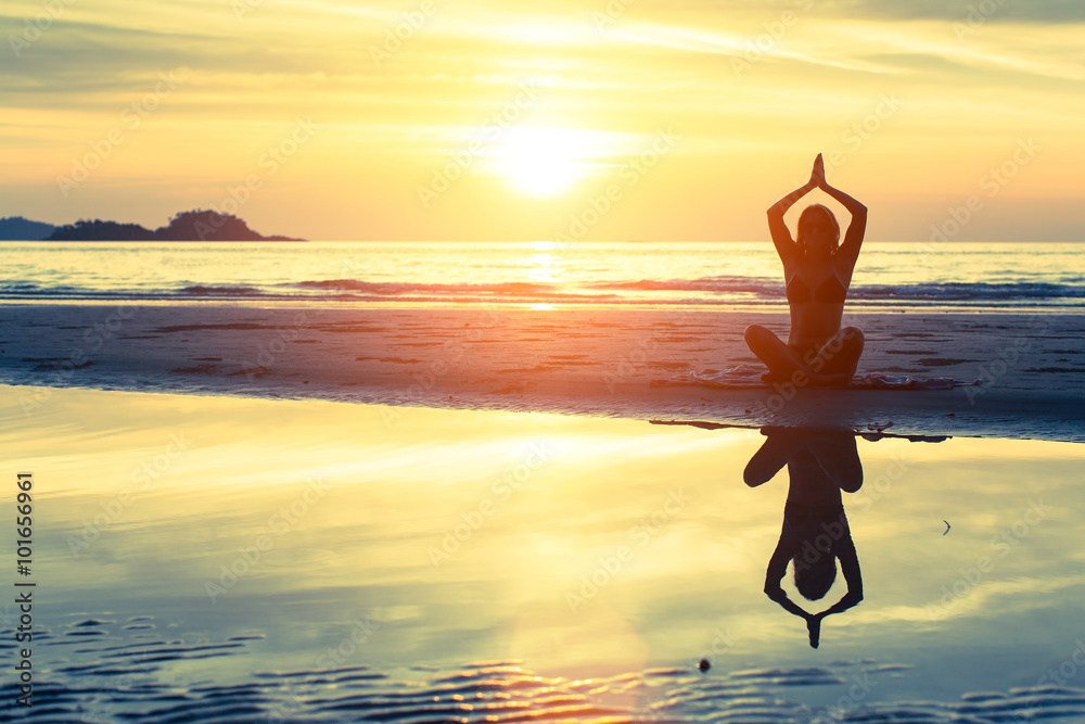 Silhouette of female practicing morning yoga exercises on a beach.