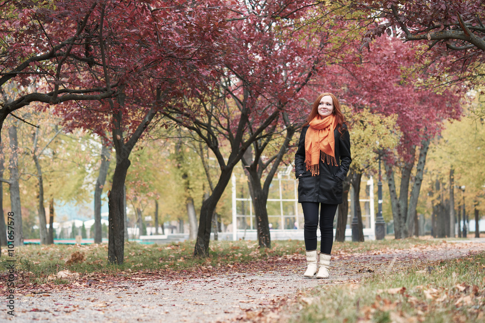 Fototapeta premium redhead girl walk on pathway in city park, fall season