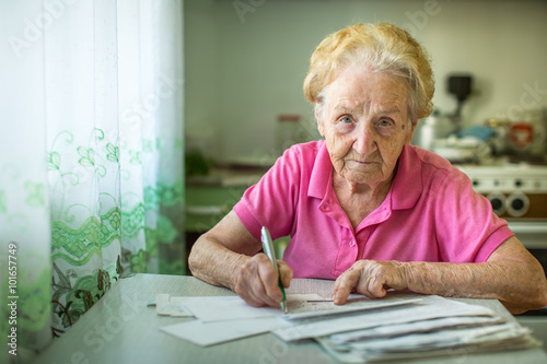 Fotografie, Obraz An elderly woman fills in utility bills.