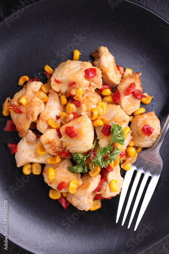 fried chicken with corn and sweet red peppers on a black plate