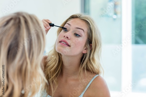 Beautiful woman putting on mascara in the bathroom