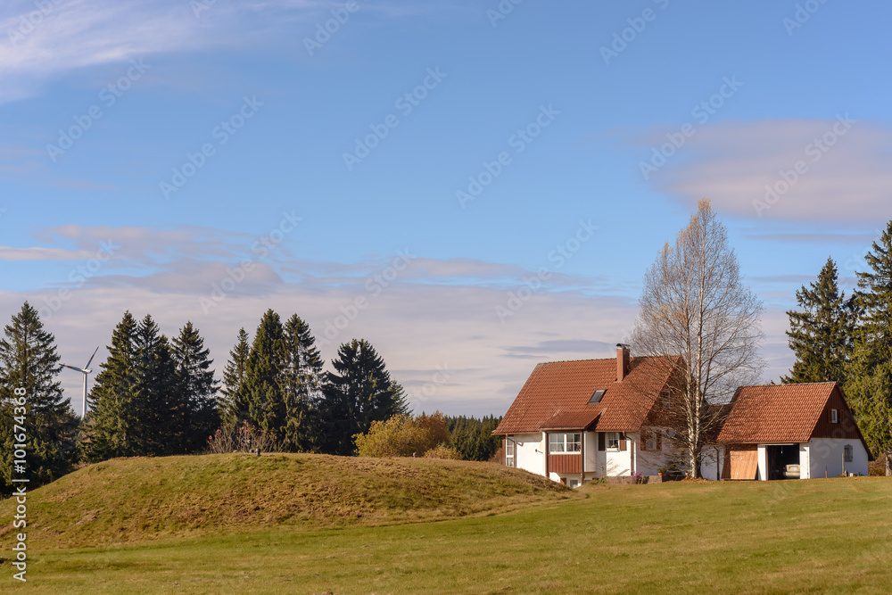 A farm is located on the green grassy hill. In the background there are mountains covered with a coniferous forest. A farm is located on the green grassy hill. In the background there are mountains covered with a coniferous forest.