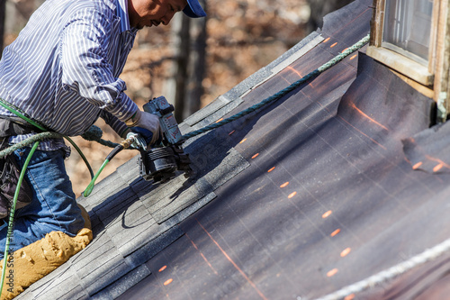 Roofer uses nail gun to secure shingles.