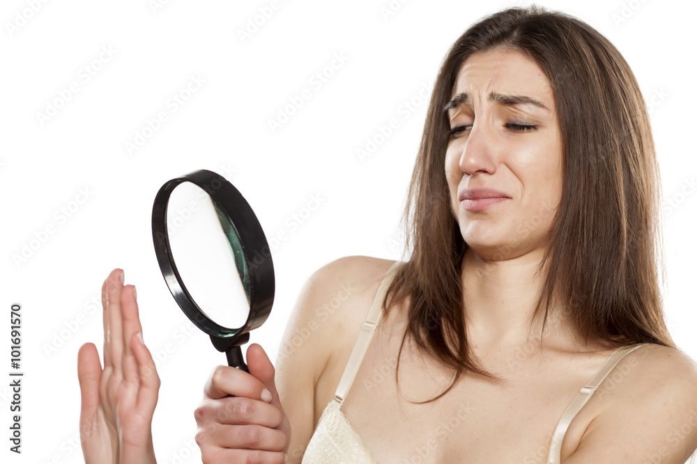 disgusted young woman looking at her nails through a magnifying glass disgusted young woman looking at her nails through a magnifying glass