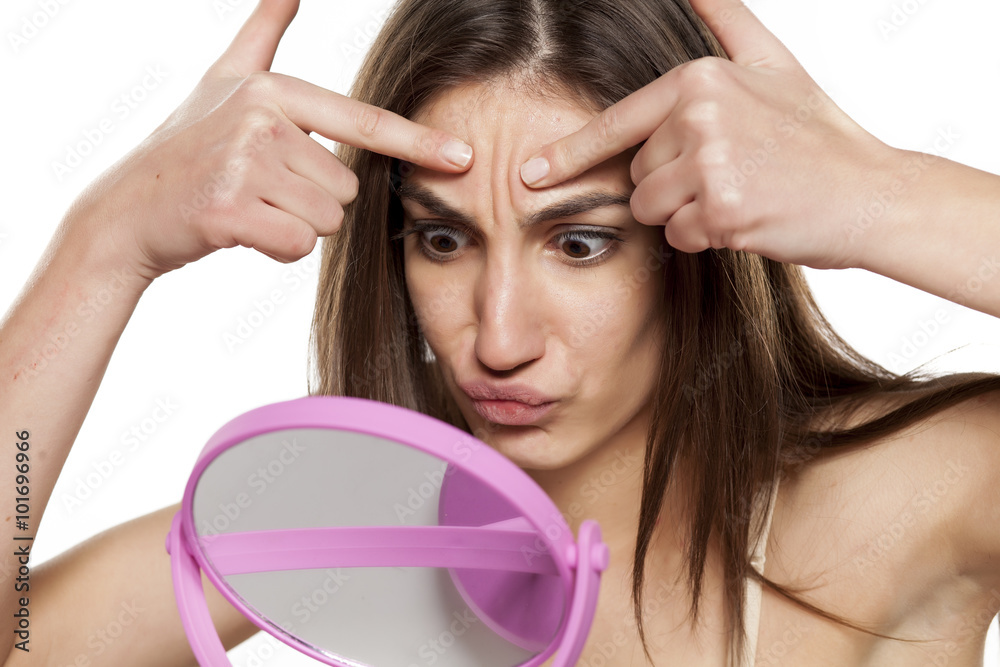 Φωτογραφία worried young woman kneading the skin on her face in front of the mirror