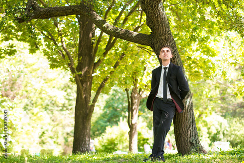 Man dressed suit stands nearthe tree photo