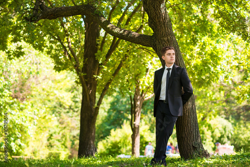 Man dressed suit stands nearthe tree © illustrissima