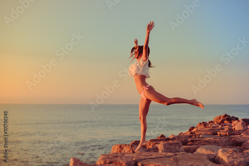 Happy girl in bikini jumping on a beach at sunset or sunrise