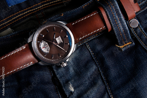 Wrist watches on brown leather strap as belt on blue jeans