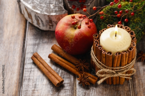 Candle decorated with cinnamon sticks and red apples