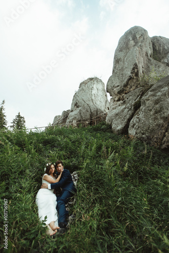 luxury happy bride and stylish groom lying on grass under sunny