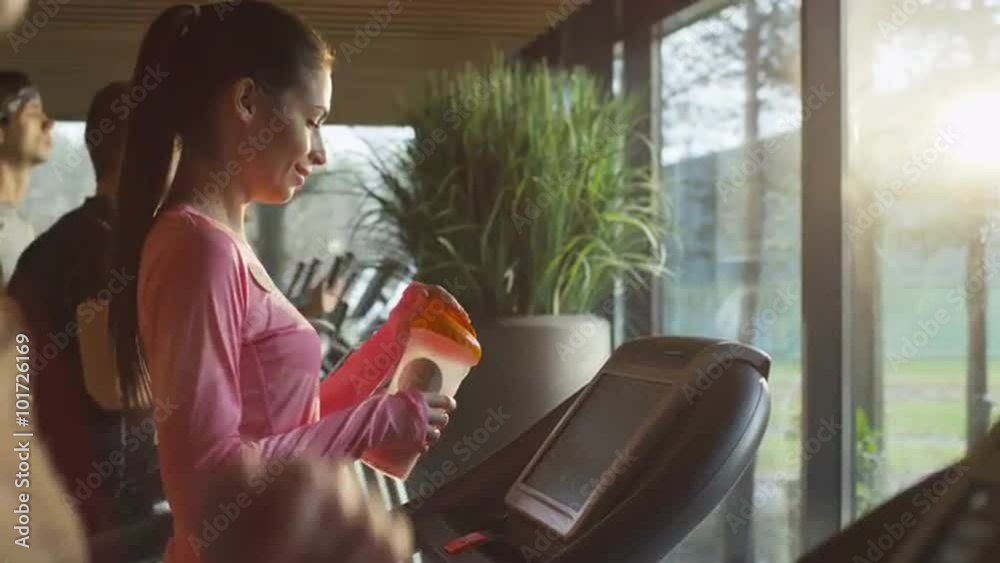 Fit athletic girl is drinking protein shake while exercising on treadmill in sport gym. Shot on RED Cinema Camera. Fit athletic girl is drinking protein shake while exercising on treadmill in sport gym. Shot on RED Cinema Camera.