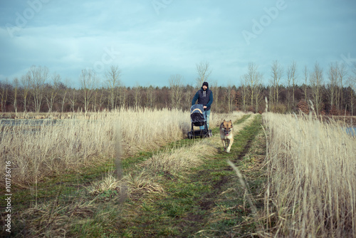 Vater geht mit Kind(erwagen) und Hund spazieren