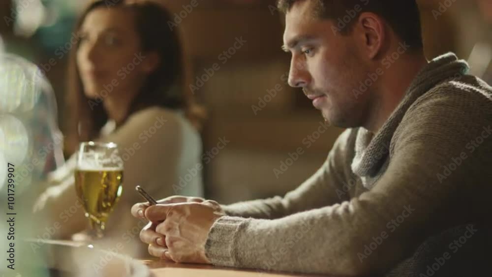 Man is typing a message on a smartphone in a bar while a glass of beer is standing on the counter. Shot on RED Cinema Camera. Man is typing a message on a smartphone in a bar while a glass of beer is standing on the counter. Shot on RED Cinema Camera.