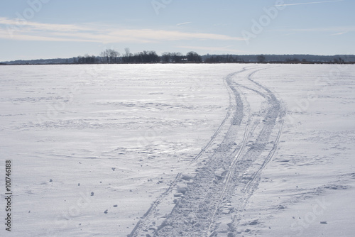 Snowmobile tracks race off to the horizon across the flat snow and ice of a lake.