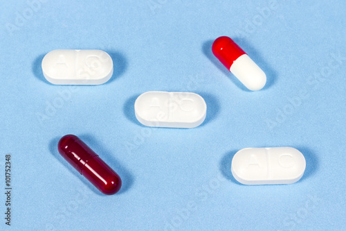 Generic tablets of clavulanic acid beside hard gelatin capsules, on blue floor. Antibiotic drugs