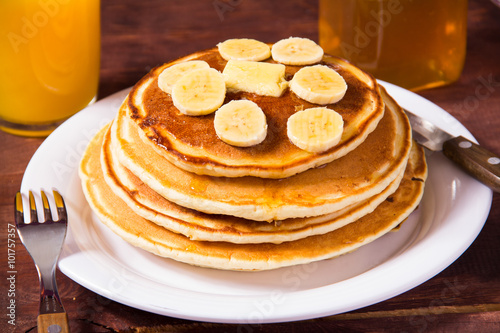Pancakes with bananas and orange juice on a wooden background