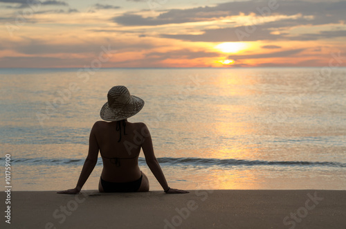 Relaxed woman watching sunset at beach seashore. Young woman enjoying summer vacation relax. photo