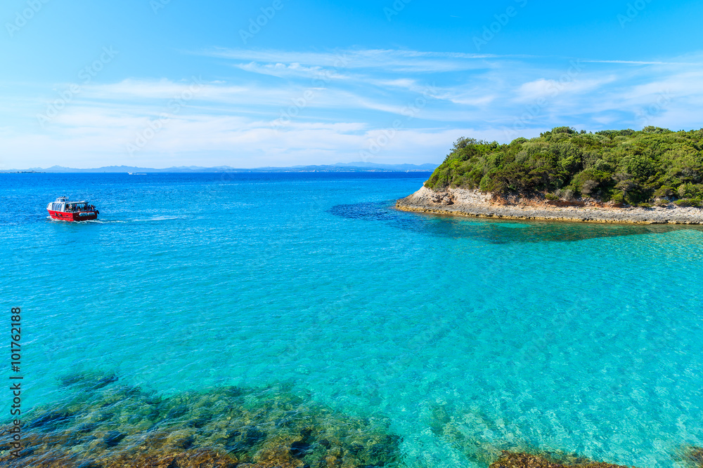 Tourist boat cruising on turquoise sea water near Petit Sperone bay, Corsica island, France