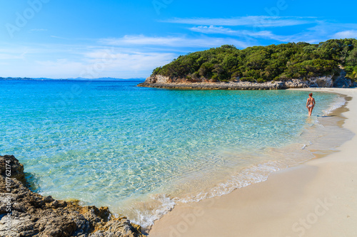 Unidentified woman walking along sandy Petit Sperone beach with azure sea water on coast of Corsica island, France