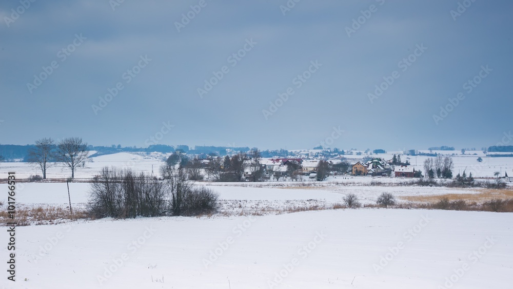 Winter field near village landscape under cloudy sky.