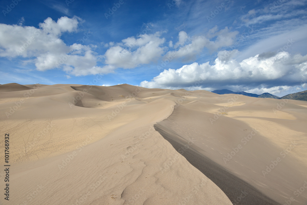 The ridge of a massive sand dune runs from the bottom of the farm into a blue sky near Sand Dunes National Park in southern Colorado.