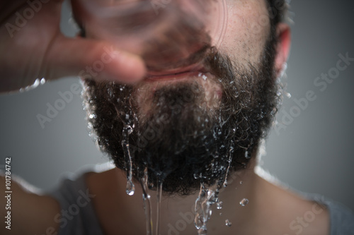 Junger Mann trinkt Wasser und macht sich dabei nass