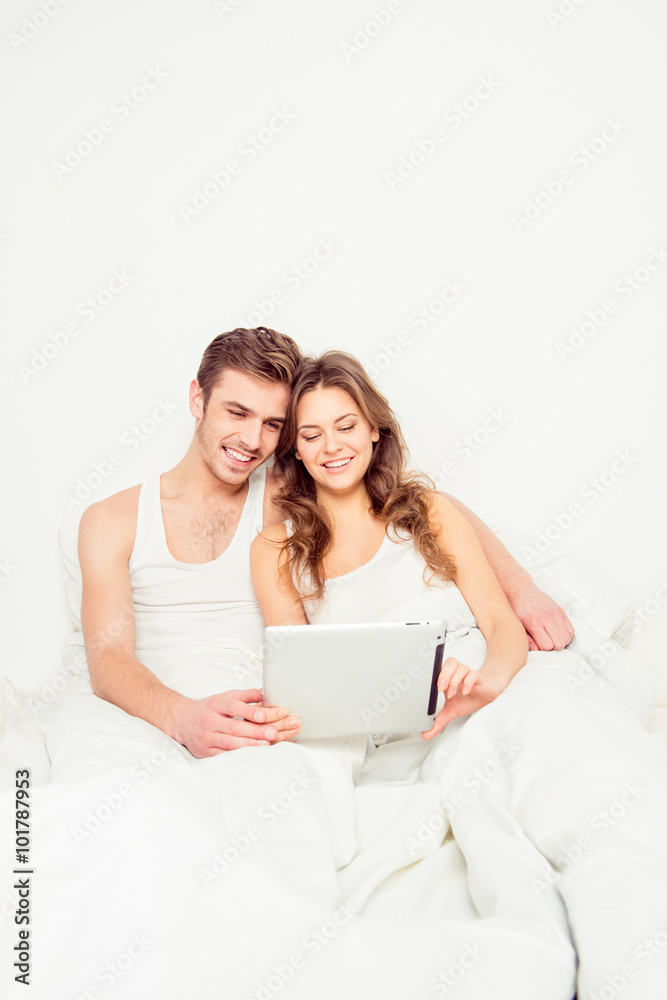 Happy couple in love sitting in bed and looking into tablet Happy couple in love sitting in bed and looking into tablet