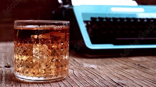 cinemagraph of some bubbles emerging in a glass with liquor placed in a rustic wooden desk with an old typewriter in the background