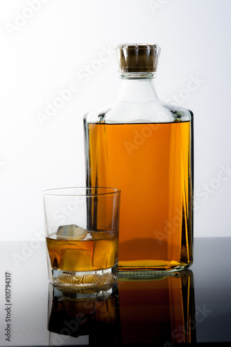 Glass and bottle with ice cubes and reflection drink alcohol on