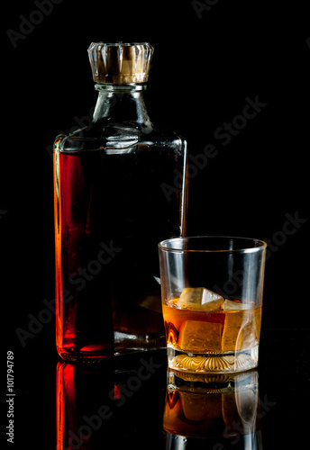 bottle and glass of whiskey with ice on dark background
