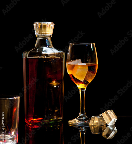 bottle and wineglass of whiskey with ice on dark background