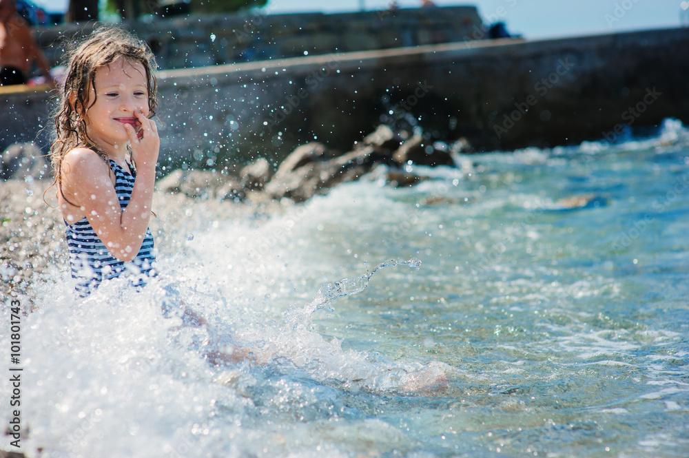 Obraz premium happy child girl in swinsuit relaxing on the beach and playing with water. Summer vacation at sea.