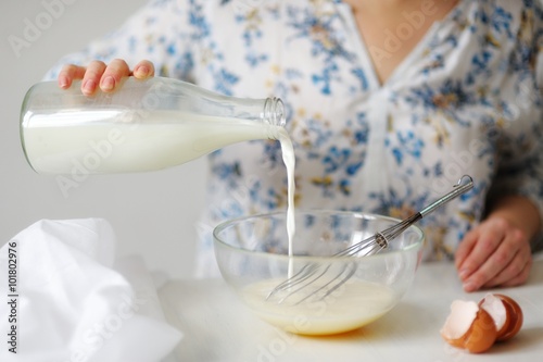 A young woman in a beaten egg mixture pours milk.