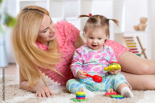 Baby playing with her mother on carpet in nursery