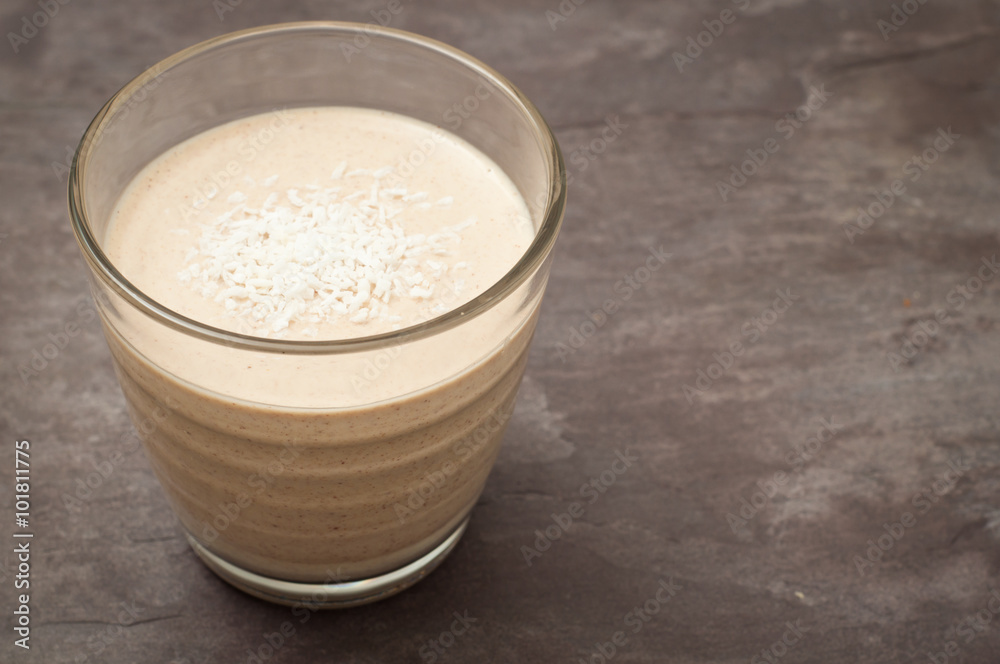Healthy peanut butter banana smoothie milkshake topped with coconut. Served on a gray stone slate background. Healthy peanut butter banana smoothie milkshake topped with coconut. Served on a gray stone slate background.
