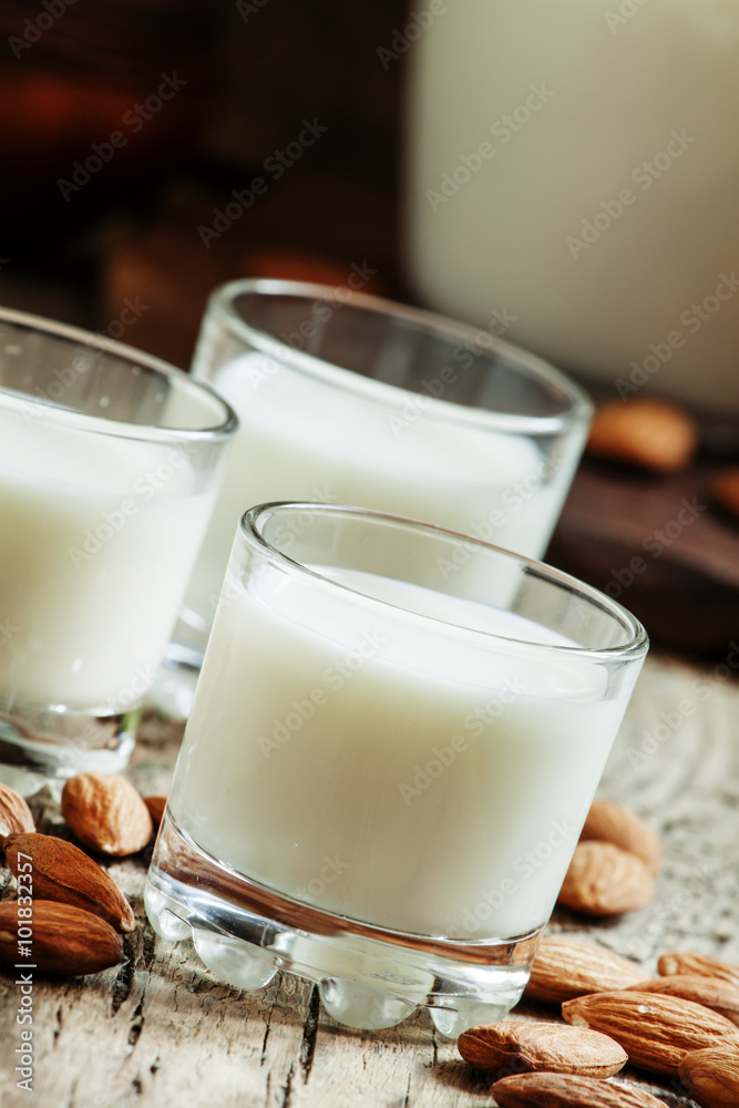 Almond milk in small glasses and spilled dry almonds on old wood Almond milk in small glasses and spilled dry almonds on old wood