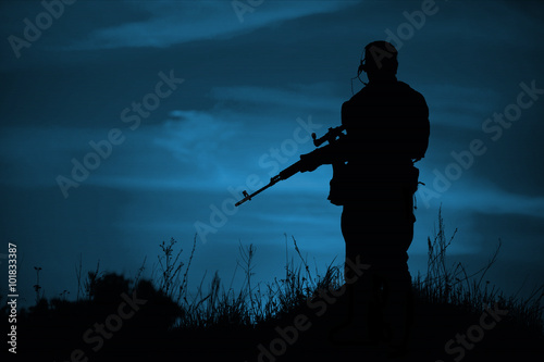 Silhouette of military sniper with weapons at night.