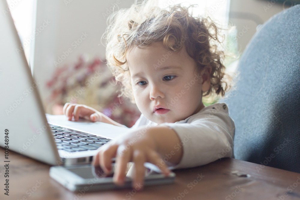 Little office worker. Toddler playing with laptop on wooden tabl Little office worker. Toddler playing with laptop on wooden tabl