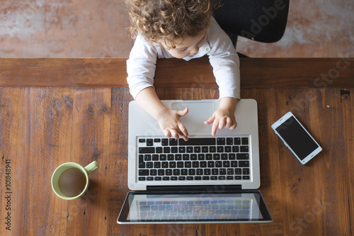Little office worker. Toddler playing with laptop on wooden tabl